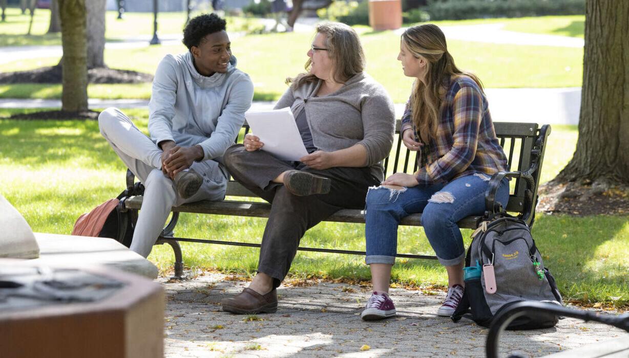 Students and a professor chat on a bench